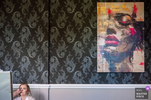 Bride Has Makeup Applied At Landgoed Wolfslaar Breda Netherlands With Striking Painting Creating Visual Contrast At Landgoed Wolfslaar in Breda, Netherlands, a bride has her makeup applied for her wedding. The minimalist shot is made richer by a large painting of a woman with heavy makeup on the wall, creating a striking visual contrast.