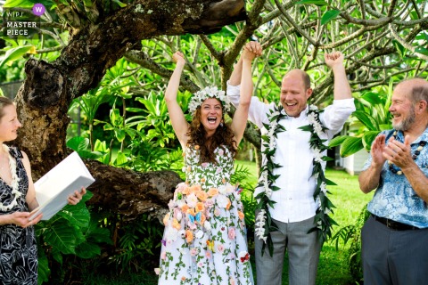 At a private estate in Oahu, Hawaii, the photographer captures a couple raising their hands in excitement at the ceremony’s end, skillfully framing the jubilant moment among gathered loved ones.