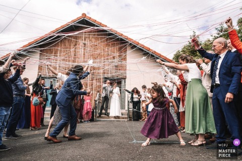 At Domaine des Plaines, France, the photographer captures guests passing balls of yarn to weave a collective web after the ceremony, expertly highlighting unity, creativity, and a poignant shared moment.