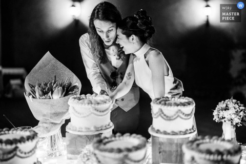Newlyweds Share Affectionate Moment During Cake Cutting At Villa Breda Cellatica At Villa Breda in Cellatica, the photographer captures the newlyweds sharing an affectionate, lighthearted moment during the cake cutting, skillfully using black and white to highlight genuine emotion and expert timing.