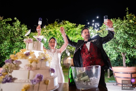 Newlyweds Raise Glasses In Celebration After Cake Cutting At La Casina Residenza di Campagna Pievedizio At La Casina Residenza di Campagna in Pievedizio, the photographer captures the newlyweds raising their glasses in celebration after cutting the wedding cake, expertly preserving joyful energy and perfect timing.