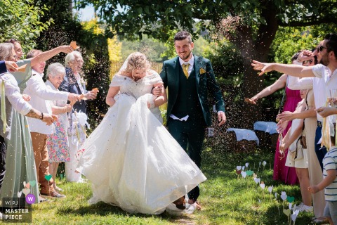 At a reception in Hérault, Occitanie, the photographer captures the bride and groom walking through a sunlit guard of honor after the ceremony, expertly highlighting joyous celebration and radiant, timely emotion.