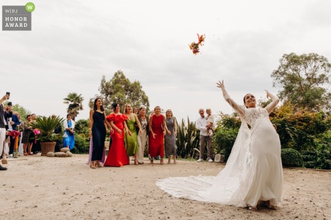 The bride tosses her colorful floral bouquet to a group of waiting guests during a joyful outdoor celebration at the historic Château les Hauts in France.