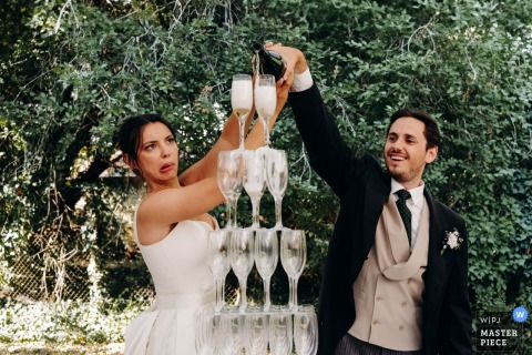 Newlyweds Pour Tower Of Glasses To Launch Cocktail Hour At Lizeray Festive Celebration At Lizeray, the photographer captures the newlyweds launching the cocktail hour by pouring a tower of glasses, expertly freezing the festive spirit and sparkling excitement of this celebratory tradition.