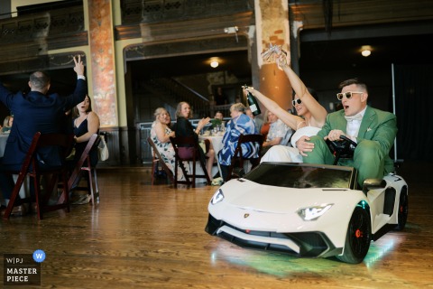 Bride and groom in a souped-up toy car, handing out champagne at Turner Hall Ballroom, Milwaukee, Wisconsin.