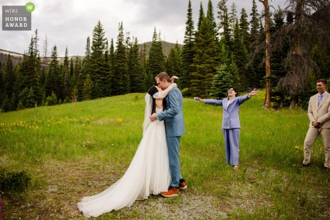 Under the vast sky of Rocky Mountain National Park, the officiant triumphantly raises her arms as the bride and groom share their first kiss as a married couple.