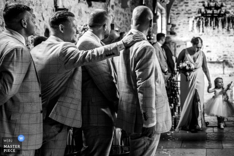 Man in suit comforting emotional groom during wedding ceremony at Healey Barn, Northumberland, UK.