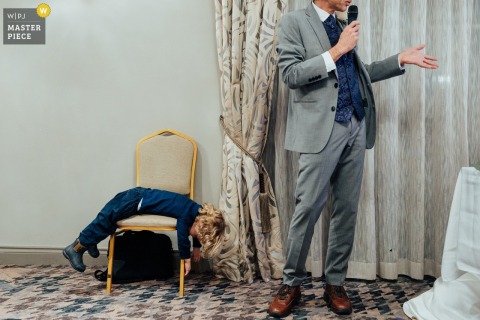 Child, laying on belly over a chair, disinterested in Father of the Bride's speech at the Nottinghamshire Golf Club, Nottingham, UK.