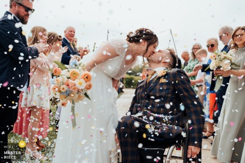 Confetti Kiss: Bride and Groom Celebrate Joyfully at Quorn Manor House Wedding At Quorn Manor House in Leicestershire, the photographer captures the bride and groom’s kiss amid a confetti shower outside, perfectly freezing a jubilant post-ceremony moment with expert attention to celebration and timing.