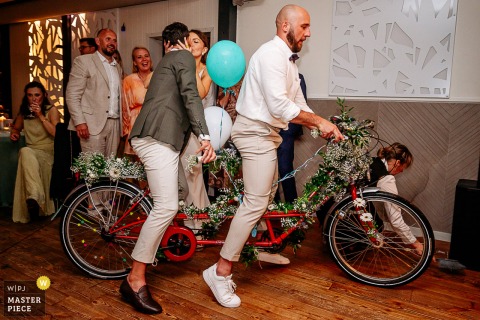 At Restauracja nad Potokiem, the photographer captures two men delivering a tandem bike as a wedding present, skillfully spotlighting whimsical celebration and the delight of unique gifts.