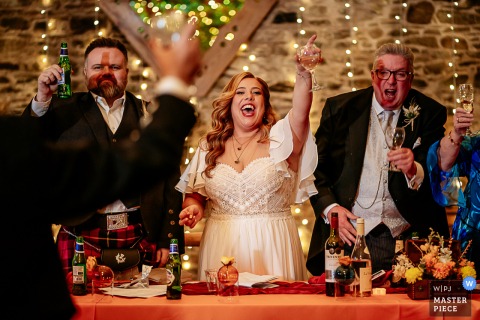 At New House Farm in England, the photographer captures the bride and groom raising glasses during speeches, expertly preserving the celebratory spirit and a heartfelt toasting moment.