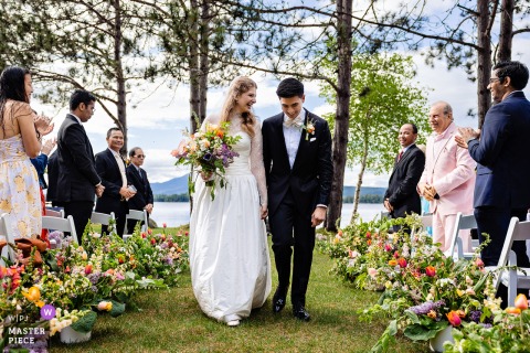 Elated Bride and Groom Walk Aisle After Outdoor Wedding at Maine’s New England Center Maine, New England Outdoor Center. Bride and groom, elated, walk down the aisle after their outdoor wedding ceremony.