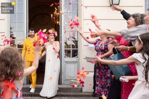 Bride Playfully Shushing Guests Tossing Petals At Saint Germain en Laye Ceremony Exit Celebration At Saint Germain en Laye, France, the photographer catches the bride playfully shushing lively guests tossing petals as the couple exits the ceremony, skillfully freezing a lighthearted, unforgettable moment of celebration.