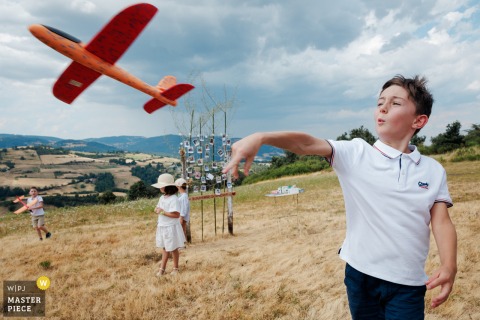 At a Rontalon reception, the photographer captures children playing with cardboard toy airplanes amid rolling hills, skillfully highlighting carefree joy and the playful spirit of the outdoor celebration.
