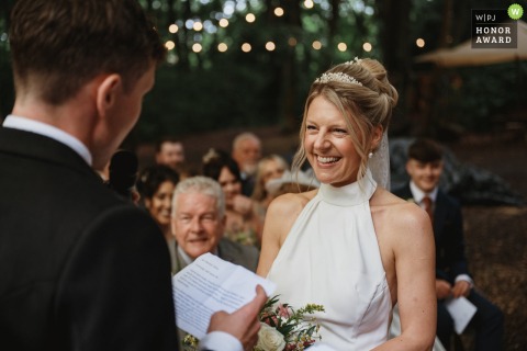 A radiant and happy bride celebrates her marriage amidst the lush greenery of a peaceful woodland wedding setting located in the scenic area of Hereford in the United Kingdom. 