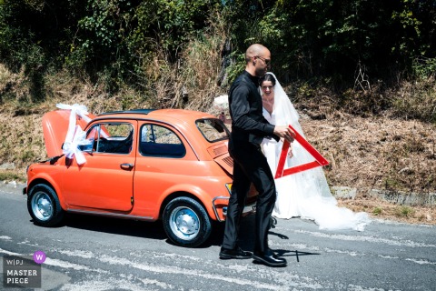 Roadside Breakdown in Ancona Becomes a Memorable Wedding Moment In Ancona, the photographer captures a unique wedding moment as the groom prepares to set out a hazard triangle beside their car, expertly turning a roadside breakdown into a memorable, story-driven image.