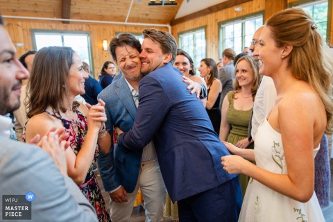 At Sugarbush Resort in Warren, Vermont, the photographer captures an awkward embrace between the groom and a guest, skillfully highlighting telling expressions and uneasy body language in a candid reception moment.