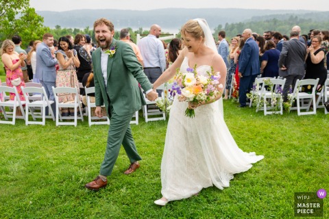 At Highland Lodge in Greensboro, Vermont, the photographer captures the bride and groom’s joyful post-ceremony reactions on the grass, holding hands, with radiant expressions, highlighting expert timing and genuine emotion.