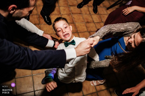 At Le Grand Hotel, Le Pont, Switzerland, the photographer masterfully captures a high-angle view of a young boy doing the limbo under guests’ arms, highlighting playful party energy and spontaneous joy.