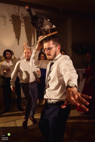 A whimsical scene at Chateau du Pin in Morancé, France, features a stuffed duck worn confidently as a hat by a guest dancing energetically on the crowded reception floor.