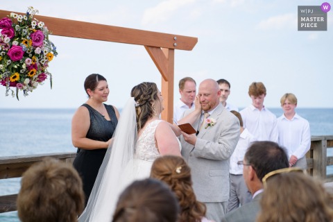 A WPJA-winning photo at Kitty Hawk Pier captures the groom’s raw emotion as he reads his vows by the water, showcasing the photographer’s timing and sensitivity to meaningful moments.