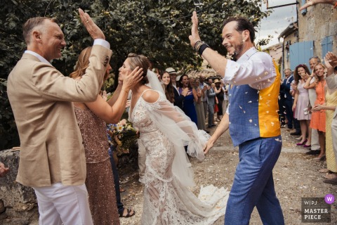 At The Castelnau, Lectoure, confetti fills the air as the bride hugs and the groom high-fives a guest. The photographer’s timing captures joyful energy and spontaneous celebration.