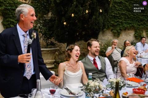 At Château de Mauriac, the bride’s father delivers a heartfelt speech, holding her hand and a mic as guests laugh. The photographer’s creative skill captures the warmth and connection of this touching family moment.