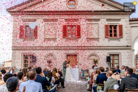 Red Confetti Showers Exiting Couple: Vibrant, Joyful Wedding Moment Captured at Villa Prato At Villa Prato, Piemonte, vibrant red confetti fills the air over the exiting couple and crowd. The photographer’s technical expertise freezes this joyful, colorful celebration in a dynamic wedding moment.