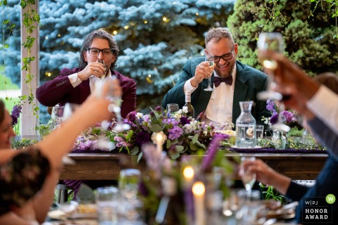 The newlyweds raise their glasses for a joyful cheers with their seated guests while a friend delivers a heartfelt toast at Tapestry House by Wedgewood Weddings in Colorado.