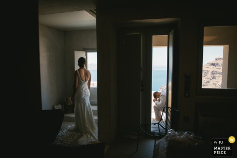 In Santorini, Greece, the bride prepares in the bathroom while the groom waits outside, carefully avoiding a glimpse to keep the wedding day surprise.