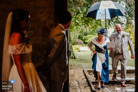 At Hooton Pagnell Hall in Doncaster, UK, the bride and groom stand together on the left, waiting as guests enter through a doorway on the right side of the frame.