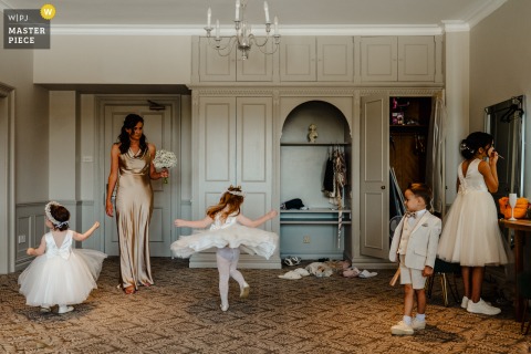 At Hartsfield Manor in Surrey, UK, four children in formal wear amuse themselves across the scene as an adult stands nearby, adding a lively touch to the wedding atmosphere.