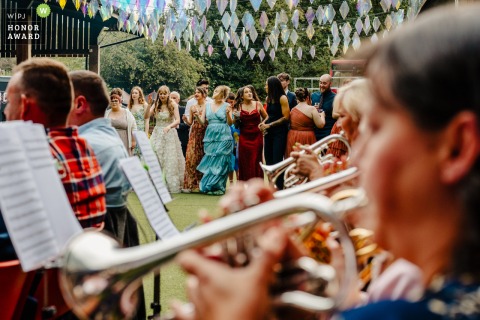 Whitebottom Farm in Stockport, UK, is filled with joyful music as a brass band plays during the wedding reception, guests mingling in the lively background.
