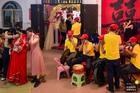 Guests And Band Members Cover Their Ears As Firecrackers Explode At A Home In Zhanjiang Guangdong At their home in Zhanjiang, Guangdong, everyone, guests and folk band members alike, instinctively covers their ears as loud wedding firecrackers crackle through the air.