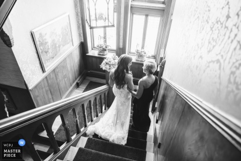 At the ceremony location in Cleveland, Ohio, the bride shares a final moment with her mother before walking down the aisle, captured in black and white from behind and above.