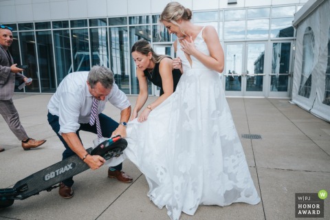 As the bride rides a scooter into the reception venue in Cleveland, Ohio, her dress becomes caught in the wheel, creating an unforgettable and unplanned entrance.