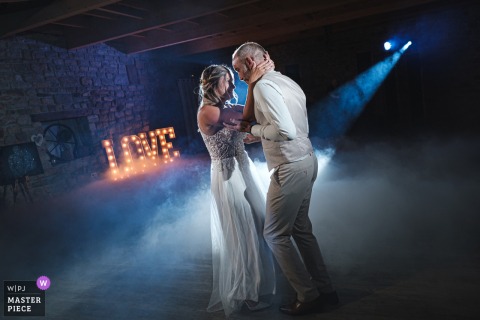 At Domaine des Rhododendrons in Quimper, Brittany, the couple shares a romantic first dance, highlighted by dramatic lighting and thick smoke on the floor, with a slight tilt to the composition.