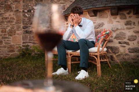 At Domaine des Cavaliers in Guidel, Brittany, a male guest sits with his hands on his face, looking weary, as a large, out-of-focus wine glass dominates the foreground of the image.