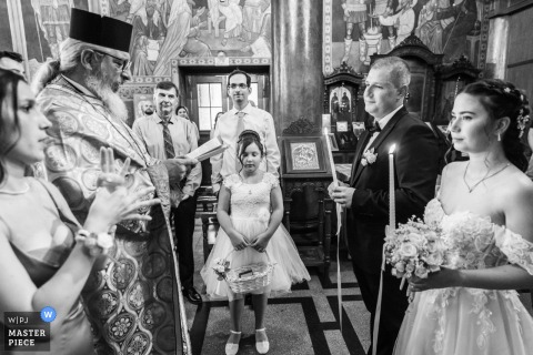 In Plovdiv, during the ceremony, a flower girl stands between the priest and the couple, adding a touch of solemn reverence to the religious celebration.