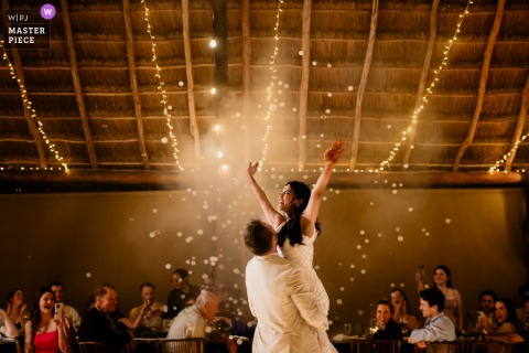 At Blue Venado in Mexico, the groom lifts the bride during their first dance grand finale, with fireworks illuminating the night and guests cheering in a warm, glowing scene.