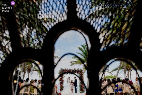 At Blue Venado in Mexico, the beach ceremony is seen from a distance, symmetrically framed through arched trellis supports, highlighting the couple against the shoreline backdrop.