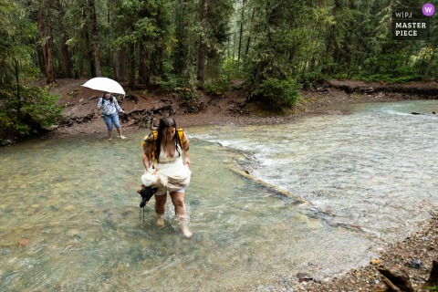 At Mineral Creek Falls in Silverton, Colorado, the brides brave icy water and heavy rain, grimacing as they ford the mountain stream together en route to their ceremony.