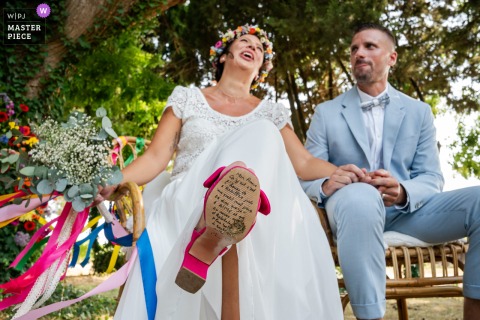 In Lunel, France, the bride sits beside the groom, revealing a special handwritten message on the sole of her shoe during the wedding celebration.