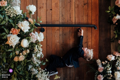 At Wharfdale Grange in Yorkshire, UK, a child playfully swings on a hand rail, surrounded by vibrant flowers during the wedding celebration.