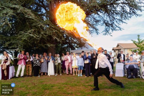 At Moulin de Trancart in Marnay, France, a wedding guest performs a fire-breathing show during the celebration, entertaining guests with a dramatic and unforgettable spectacle.