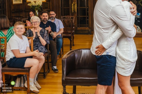 A Couple Shares A Warm Embrace During Their Wedding Ceremony Inside Nottingham Council House In Nottinghamshire Inside Nottingham Council House, a couple shares a warm embrace during their ceremony with guests clapping, smiling, and celebrating the happy occasion.