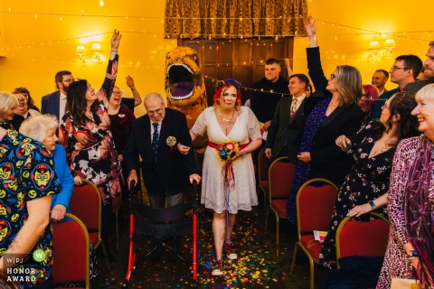 Bedford Hall Thorney features a memorable entrance as the bride is escorted by her future father-in-law and a whimsical dinosaur, while laughing guests hold up fairy lights to help them through.