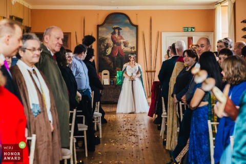 At Holme Pierrepont Hall, the bride stands patiently with a sword in hand, awaiting her walk down the aisle as intrigued guests watch the unconventional moment unfold.