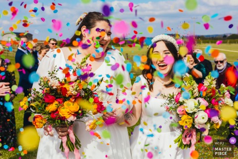 At The Old Cow Shed, the newly married couple walks through a shower of colorful confetti as guests celebrate their wedding in a joyful, vibrant moment.