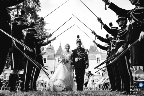 At Château Marith in Lot-et-Garonne, France, the newlyweds exit their secular ceremony beneath an honor guard arch of sabres and military uniforms, celebrating tradition and union.